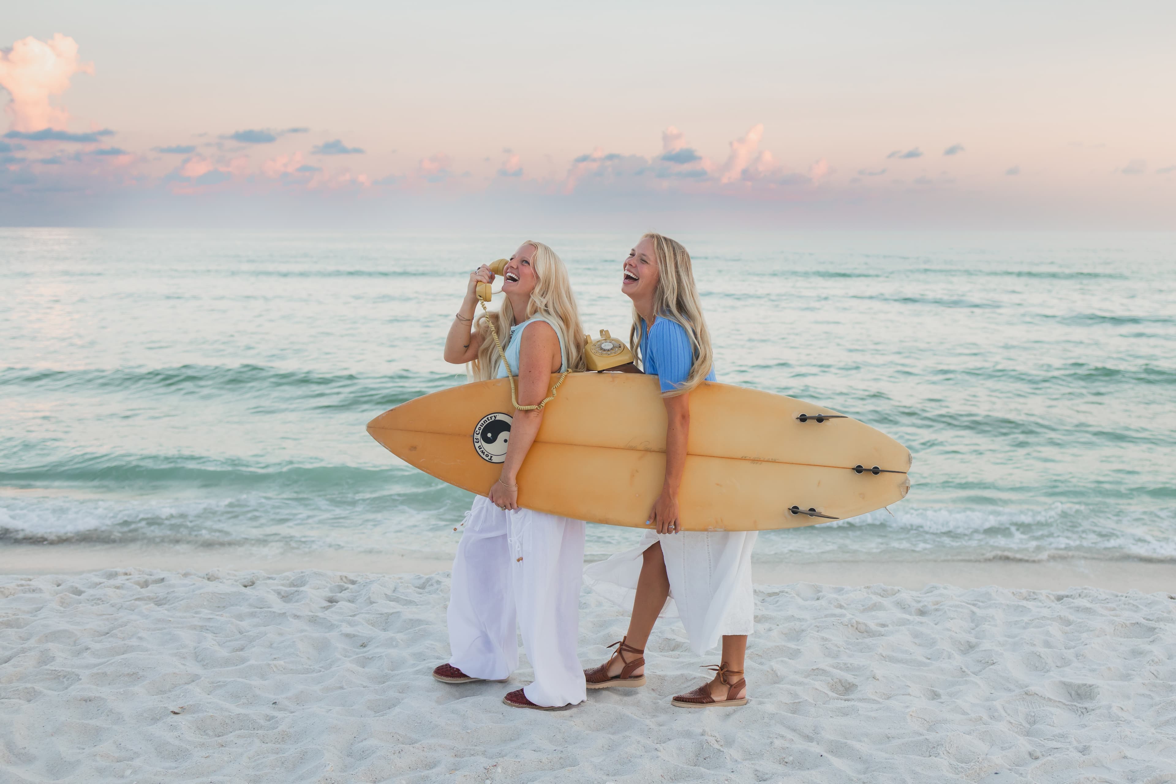 Aly and Jordan of Palm Media carrying a surfboard on the beach